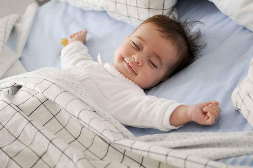 Smiling baby girl lying on a bed sleeping on blue sheets